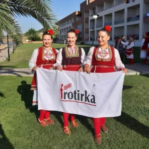 Три девојки од КУД Гоце Делчев Делчево во традиционални македонски носии држат крпа со логото на Фротирка на Интернационалниот фолклорен фестивал ТУФАГ 2019 во Турција.