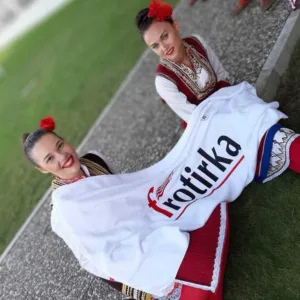 Две девојки од КУД Гоце Делчев Делчево во народни носии држат крпа со логото на Фротирка на фестивалот ТУФАГ 2019 во Турција.