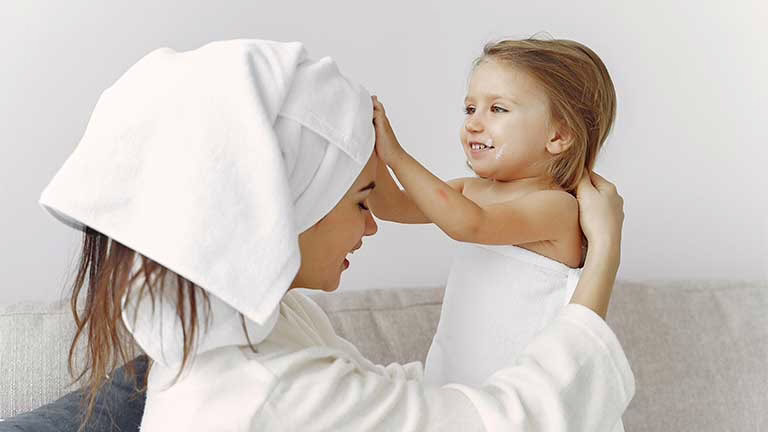 Мајка и дете завиткани во меки бели пешкири за бања, симбол на хигиенска и безбедна грижа за бебешки и детски крпи.