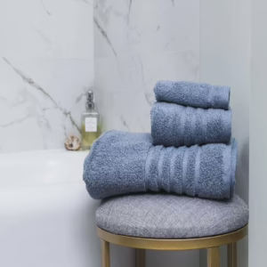 Сет од три сини пешкири за бања поставени на столица покрај када.