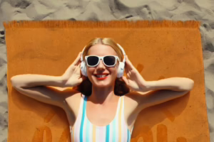 Жена со костим за капење и слушалки лежи на портокалова плажна крпа на песок – летна релаксација со стил од Frotirka.